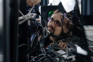 Seorang siswa TKJ sedang melakukan troubleshooting pada perangkat jaringan komputer dan telekomunikasi, memeriksa kabel dan konfigurasi.